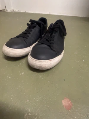 Svarta sneakers med vit sula - Klassiska svarta sneakers med vit, något tjockare sula och snörning. Skorna har en stilren och enkel design i skinnimitation och passar perfekt till jeans eller shorts. Låg modell med rund tå och svart ovandel.