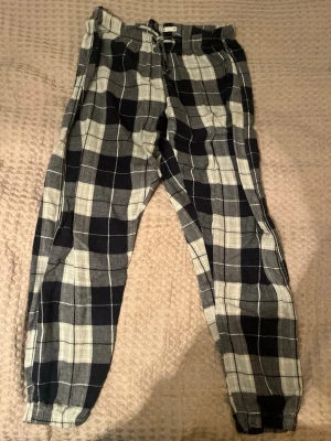 Svarta, grå- och vitrutiga mjukisbyxor - Rutiga mjukisbyxor i svart, grått och vitt från Cubus, storlek M. Byxorna har elastisk midja med snörning och muddar vid bensluten. Perfekta för chill dagar och har en loose passform. Materialet känns mjukt och bekvämt mot huden.