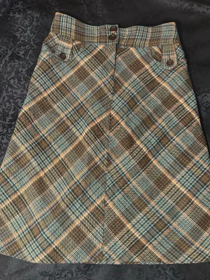 H&M Rutig brun och blå kortkjol XS( 34) - Säljer en snygg A-linjeformad kjol med rutigt mönster i brunt, blått, beige och orange. Kjolen har hög midja, knappdetaljer och bälteshällor. Materialet är tjockt och känns som ull, perfekt för dig som gillar retrovibbar och coola detaljer. 50% bomull, 25% akryl, 25% polyester. Midjemåttet 68cm