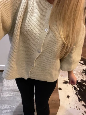 Beige stickad kofta med knappar - Mysig beige stickad kofta från designed by si med rund hals och knäppning framtill. Perfekt till kallare dagar och säljer då den inte kommer till användning.