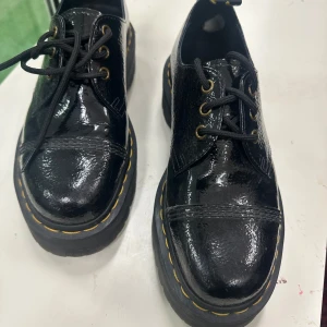 Dr. Martens 1461 Quad svart lack - Säljer ett par Dr. Martens 1461 Quad i svart lack med chunky plattformssula och gula sömmar. Skorna har snörning, rund tå och klassisk Dr. Martens-flärp bak. Tillverkade i glansigt skinn och har robust gummisula.