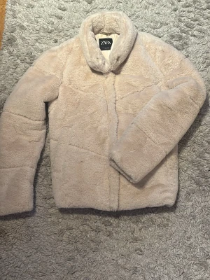 Beige teddyjacka från Zara - Säljer en fluffig och supermjuk teddyjacka från Zara i beige färg. Jackan har en klassisk krage och är gjord i ett pälsliknande material som känns riktigt cozy. Den är knappt använd och säljer för att den inte riktigt passar mig. Eftersom den knappt är använd är pälsen i super bra skick. Den är dock lite kortare i ärmarna och inte så stretchig. Köparen betalar frakten. 