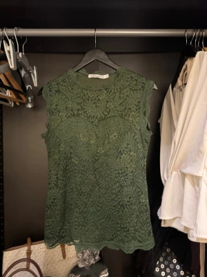 Grön spetsblus från Copenhagen Luxe - Supersnygg grön blus i spets från Copenhagen Luxe. Ärmlös modell med rund hals och detaljerat blommönster i spetsen. Perfekt att styla med jeans eller kjol för en trendig look.