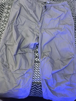 Grå cargopants med snörning - Säljer ett par grå cargopants med elastisk midja och snörning. Byxorna har flera fickor på benen och är tillverkade i ett lätt syntetmaterial som känns luftigt. Perfekta för en chill och avslappnad stil. Säljer pga att jag bytt stil. 