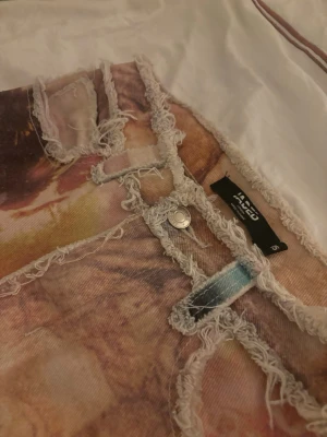 Patchwork jeans från Jaded London - Unika patchwork jeans från Jaded London med råa kanter och flera färgstarka tryck, bland annat Empire State Building och ansikten. Byxorna har raka ben, fem fickor och coola kontrastsömmar. Materialet är kraftig bomull med tryckt mönster i beige, blått, rött och brunt.