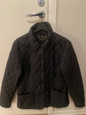 Quiltad Barbour jacka mörkblå - Quiltad mörkblå jacka från Barbour med tryckknappar framtill och två stora fickor.