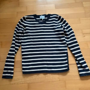 Randig stickad tröja från Ganni - Snygg stickad tröja från Ganni med marinblå och vita horisontella ränder. Modellen har rund hals och långa ärmar, perfekt för dig som gillar klassisk men trendig stil. Ribbad struktur ger extra känsla och passformen är normal.