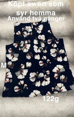 Blommig ärmlös linnetopp marinblå - Snygg ärmlös linnetopp i marinblått med stora blommiga mönster i vitt, beige och rött. Toppen har rak passform och rund halsringning. Perfekt för dig som gillar unika plagg med färg och mönster.🌸Köpt av en som syr så står inga lappar. Köpt som stl M. Använd två gånger