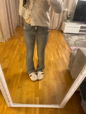 Grå bootcut jeans från Ginatricot - Snygga grå jeans från Ginatricot med bootcut passform och låg midja. Jeansen har klassiska fem fickor, dubbla knappar i midjan och dragkedja. Materialet är stretchigt jeans och färgen är en cool, tvättad grå ton.