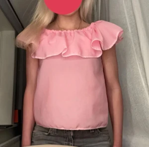 Rosa offshoulder volangtop - Säljer en ljusrosa offshoulder topp med bred volang runt hela halsringningen. Toppen kan bäras på flera sätt: offshoulder, oneshoulder eller med volangen över axlarna. 