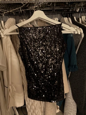 Svart glittrig paljett-topp - Säljer en svart glittrig topp med paljetter och smala axelband. 
