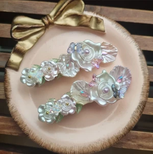 Pärlemorskimrande hårspännen  - Ett par vackra hårspännen dekorerad med blommor, pärlor och små fjärilar. Längd 5,5 cm. Jag erbjuder presentinslagning. Bara säga till! 