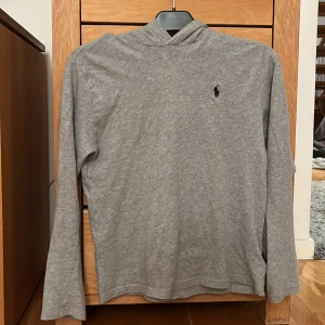 Polo Ralph Lauren hoodie - Säljer en stilren grå hoodie från Ralph Lauren, hoodien är en tunnare variant som är perfekt på sommaren. Den har bra skick och inga skador bara använd. Skriv om du har några funderingar!