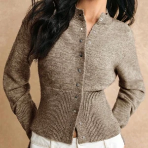 Beige ribbad kofta med knappar - Snygg beige kofta med ribbad midja och ärmslut, designad med rund hals och knappar hela vägen framtill. 