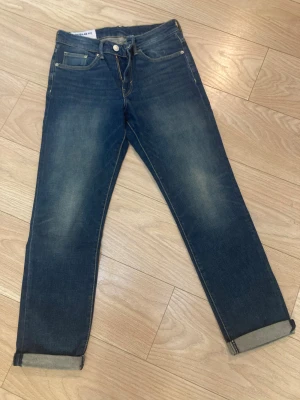 Blå jeans från H&M regular fit - Mörkblå jeans från H&M i regular fit med klassisk femficksdesign och uppvikta benslut. Jeansen har en lätt tvättad look och är tillverkade i bomull med lite stretch för extra komfort. Perfekta för en avslappnad stil.