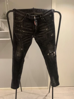 Svarta skinny jeans från dsquared2 - Svarta jeans från dsquared2 med skinny passform och slitna detaljer, hål och blekta partier för en rå och edgy look. Klassisk femficksmodell med dragkedja och knapp. Perfekt för dig som gillar streetstyle och vill sticka ut. Storlek 46 ! Hålet där fram som man ser på bilden och så är dragkedjan lite slapp men det är nog lätt att fixa annars inga problem eller fel på dom.