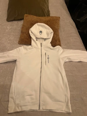 Vit zip hoodie från Sail Racing - Fräsch vit ziphoodie från Sail Racing med huva och snygga detaljer. Jackan har dragkedja framtill, snörning i huvan. Perfekt för dig som gillar stilren och sportig look. Logga på bröstet och huvan ger extra karaktär.