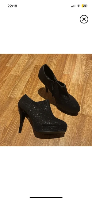 Svarta glittriga stövletter med klack - Snygga svarta stövletter med glittrig yta och hög klack. Skorna har spetsig tå, plattform och dragkedja på sidan för enkel påtagning. Perfekta för dig som vill sticka ut med lite extra glam. Materialet är syntet och de har en elegant, smal siluett. Perfekt till jul o nyår🙂