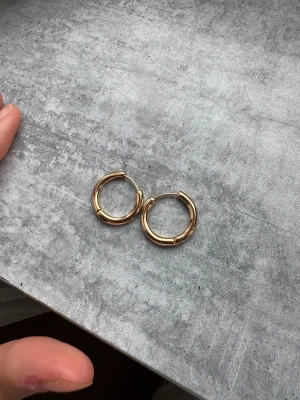 Guldiga chunky hoops örhängen - Säljer ett par snygga chunky hoops i guldfärgad metall. De är runda och har en stilren, blank finish som ger en cool vibe. Perfekta för att lyfta din look med lite extra bling. Passar dig som gillar minimalistisk men ändå trendig stil. Helt oanvända