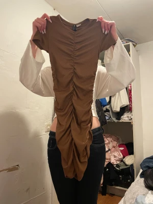 Brun ribbad kortklänning från Divided HM - Snygg brun kortklänning från Divided i ribbad bomull med tight passform. Klänningen har korta ärmar och cool rynkning längs hela framsidan som ger en unik look. Perfekt för dig som gillar trendiga detaljer och vill sticka ut lite extra.