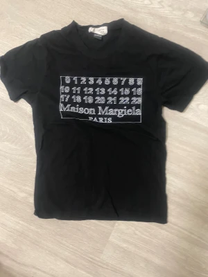 Maison Margiela svart t-shirt - Svart t-shirt från Maison Margiela med ikoniskt siffertryck och logga på bröstet.  Passar för dig som är 160-170cm lång storleken är xs. Den är jätte bra skick ingen defekter eller hål. Pris går att diskuteras vid snabbaffär. Hör av mig vid minsta lilla fundering.