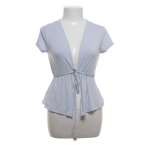 Ljusblå omlottopp från Gina Tricot - Supersöt ljusblå omlottopp från Gina Tricot med korta ärmar och knyt i midjan. Toppen har en v-ringad design och är tillverkad i mjuk bomull. Två första bilderna är gamla, den hade ett hål i ryggen på ca 1 cm som är sytt så det syns inte att det är sytt eller varit ett hål där (se sista bilden). 🩷 