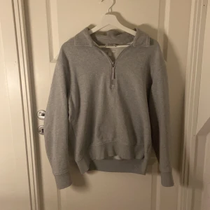 Grå half zip sweatshirt från COS - Grå sweatshirt från COS med half zip framtill och hög krage. Tröjan har långärmad design, ribbade muddar och är tillverkad i mjuk bomull. Perfekt för chill dagar och enkel att matcha med jeans.