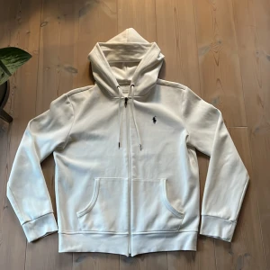 Vit ziphoodie från Ralph Lauren - Snygg vit zip från Ralph Lauren med klassisk broderad logga på bröstet. Tröjan är i storlek S med normal passform. Tröjan har en liten defekt på ryggen som syns på bild, skulle säga att skicket ändå är 8/10. Hör gärna av er vid mer frågor!🏌️