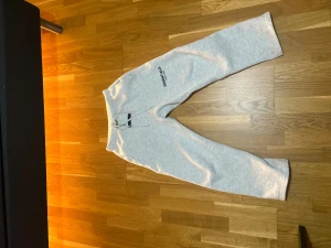 Grå mjukisbyxor Essentials S - Snygga ljusgrå mjukisbyxor från Essentials, Fear of God. Byxorna har elastisk midja med snörning och tryckt logga på vänster lår. Tillverkade i mjuk bomull och polyesterblandning för extra comfort. Perfekt för chill eller streetwear.