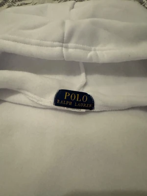 Vit Polo Ralph lauren kofta  - Vit hoodie från Polo Ralph Lauren med dragkedja och klassisk broderad logga på bröstet. Tröjan har huva, två fickor framtill och är tillverkad i mjuk bomull. Perfekt för dig som gillar clean och stilren look.