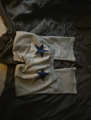 Grå mjukisbyxor med stjärnor Junkyard - Grå mjukisbyxor från Junkyard i storlek XS. Byxorna har två mörkblå stjärnor på benen och snörning i midjan. Bootcut modellen. Pris är diskutabelt.