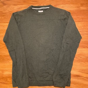 Mörkgrön tröja från Made in the Shade - En enkel och stilren mörkgrön tröja från Made in the Shade i storlek S. Tröjan har rund hals, långa ärmar och ribbade muddar vid hals, ärmslut och nederkant. Perfekt för dig som gillar basic och clean look.