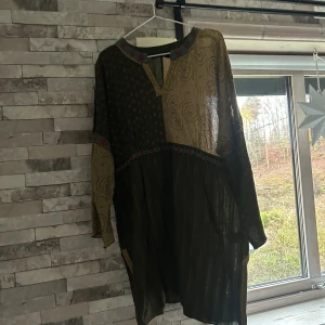 Mönstrad långklänning Gudrun Sjödén - Unik långklänning från Gudrun Sjödén i grönt och beige med broderade detaljer och mixade mönster. Klänningen har lång ärm, v-ringad hals och coola prickar samt blommor. Materialet är lätt och luftigt, perfekt för dig som gillar boho-vibe och färg.