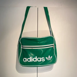 Vintage Adidas axelväska  - Hej, säljer en schysst axelremsväska från Adidas i grön/vit färg. Välanvänd med defekter, bild i dm. Dragkedjahållare borta.  Praktisk med många fack och inte för stor. Sliten. Köptes i London för ca 700kr. Pris är inte hugget i sten. Hör av dig vid frågor! 