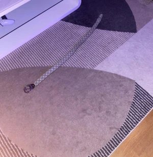 Gucci bälte med silverfärgat spänne - Säljer ett snyggt Gucci bälte med klassiskt GG-mönster i grått och beige. Bältet har ett rundat silverfärgat spänne med GG-logga och är tillverkat i skinn. Perfekt accessoar för att lyfta din outfit med en lyxig touch.