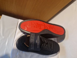 Christian Louboutin svarta sneakers 44 - Svarta sneakers från Christian Louboutin med klassisk snörning och rund tå. Ovandelen är i mocka och skinn, Yttersulan är röd med Louboutin-logga, vilket ger en lyxig och unik touch.