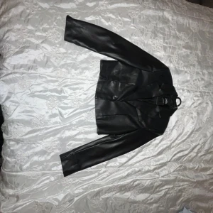 Svart skinnjacka från Zara - Snygg svart skinnjacka från Zara med klassisk krage och knäppning framtill. Jackan är croppad och har långa ärmar. Perfekt för dig som vill ha en stilren och trendig look.PRIS GÅR ATT DISKUTERAS