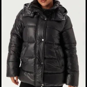 Svart pufferjacka med huva - Säljer en svart pufferjacka med huva och stora, quiltade partier. Jackan har dragkedja och tryckknappar framtill samt två sidofickor. Inga defekter, ordinarepris 899kr säljer för 200kr 