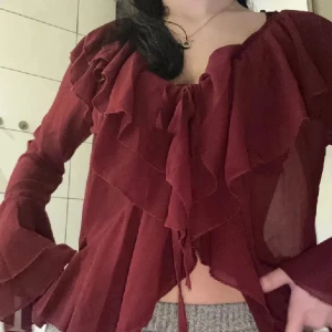 Perfekta Jul/Nyårsblusen💕 - Supersnygg vinröd blus med volanger och v-ringning. Långa, vida ärmar med vilanger och knytning framtill ger en romantisk vibe. Tunt, lätt material som faller fint och känns luftigt. Perfekt för dig som vill sticka ut med en elegant och trendig look. Strl M men sitter super på xs/s se bilderna🙂 Superfin till middag fest jul/nyår🥂🥂