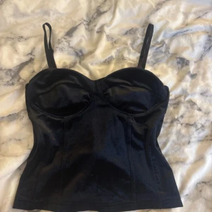 Svart sammet korsett/ topp med dragkedja - Snygg svart korsettopp i mjuk sammet med formade kupor och justerbara axelband. Toppen har en dragkedja i ryggen som gör den enkel att ta på och av. Perfekt för att skapa en cool och trendig look. Fest topp