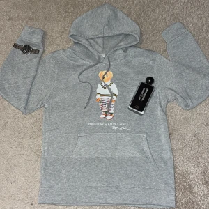 Grå hoodie Polo Bear Ralph Lauren - Grå hoodie från Ralph Lauren med Polo Bear-tryck på bröstet. Tröjan har huva med snörning, stor magficka och långa ärmar. Materialet är mjuk bomull och passformen är normal. Perfekt för dig som gillar klassisk streetstyle med en twist. OBS! (skriv innan ni hade tänkt köpa för ytterligare information)👍😁