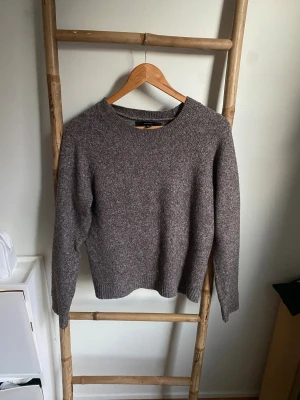 Brun stickad tröja från Vero Moda - Mysig brun stickad tröja från Vero Moda i storlek S. Tröjan har en klassisk rund halsringning och långa ärmar med ribbade muddar vid ärmslut och nederkant. Perfekt för att hålla värmen under kyliga dagar och passar till jeans eller kjol.