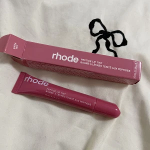 Rhode Peptide Lip Tint 'Salty Tan' - Rhode Peptide Lip Tint i färgen 'Salty Tan', ett läppbalsam med peptider som ger en mjuk och återfuktad känsla samt en naturligt rosabrun ton. Tuben är smidig och har en modern design i plast, perfekt att ha med sig i väskan.
