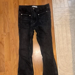 Svarta bootcut jeans - Snygga svarta jeans med bootcut passform och klassiska fem fickor. Jeansen har silverfärgade nitar vid fickorna och är tillverkade i ett slitstarkt denimtyg. Perfekta för dig som gillar en lite retro vibe och vill ha ett par jeans som sticker ut.