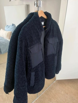 Fleecejacka  These Glory Days - Säljer en marinblå fleecejacka från These Glory Days i storlek medium. Jackan har fluffig yta, två stora fickor med lock framtill och dragkedja hela vägen upp. Materialet är mjukt fleece och syntet, perfekt för kyliga dagar. Snygg och enkel att matcha med jeans. Knappt använd som ny