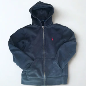 Ralph Lauren zip hoodie - Svart zip hoodie från Polo Ralph Lauren med röd logga. Tillverkad i mjuk bomull och passar perfekt till en chill och stilren look.