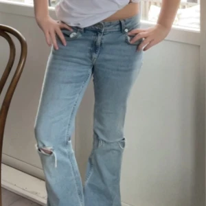 Blåa bootcut jeans med hål! - Snygga ljusblå jeans med bootcut passform och hål vid knäna. Knappast andvända, kanske 2-3 ggr. Stora i storleken så passar ungefär S-M. 
