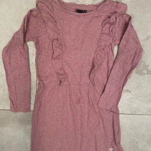 Rosa volangklänning från Hummel - Supersöt rosa klänning från Hummel med långa ärmar och volangdetaljer längs framsidan. Mjuk bomullsmix. 