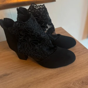 Svarta spetsiga stövletter med broderi - Unika svarta stövletter med rund tå, klack och snygg spetsdetalj med blommigt broderi. Dragkedja baktill och klacken är dekorerad med små svarta pärlor för extra edge. Perfekt för dig som vill sticka ut med din stil.