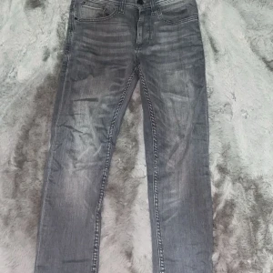 Grå slim fit jeans Jet W27 L30 - Snygga grå jeans från Jet i slim fit-modell. De har klassisk femficksdesign, subtila slitningar och kontrastsömmar. Passformen är smal och längden är 30 tum. Perfekta för dig som gillar en modern och stilren look.